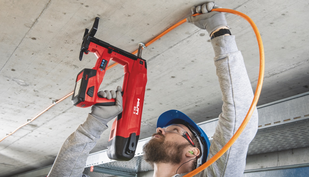 Un ouvrier fait une fixation de gaine électrique au plafond à l'aide du cloueur BX 3