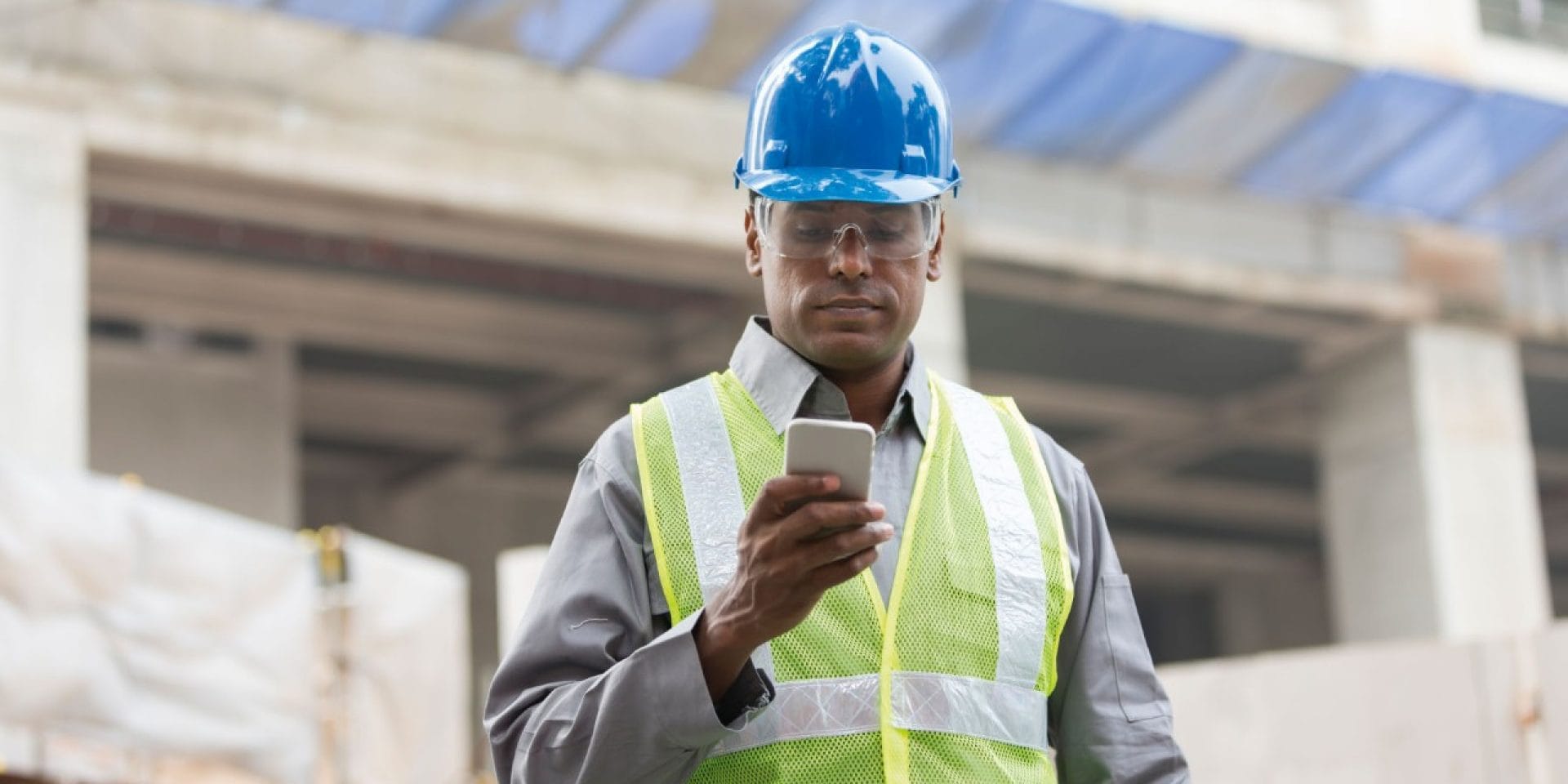 Un homme sur chantier consulte son smartphone dans sa main