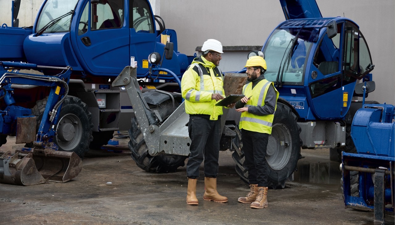Twee arbeiders praten naast een zware machine