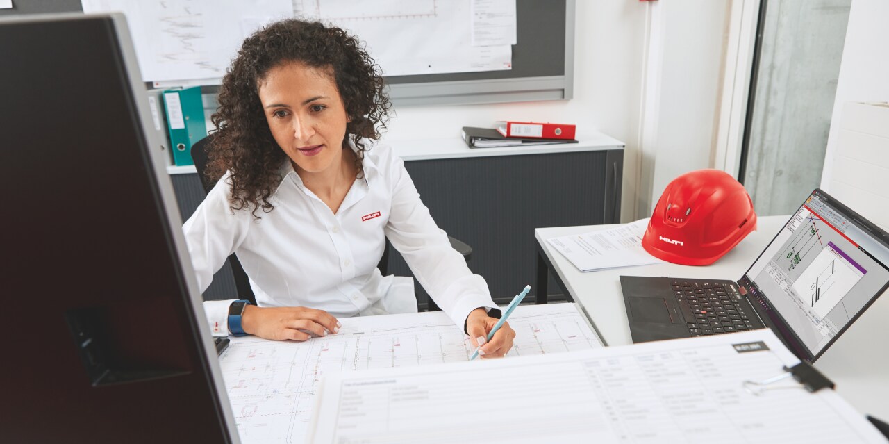 Hilti ingenieur op locatie met een klant met bouwtekeningen op de voorgrond